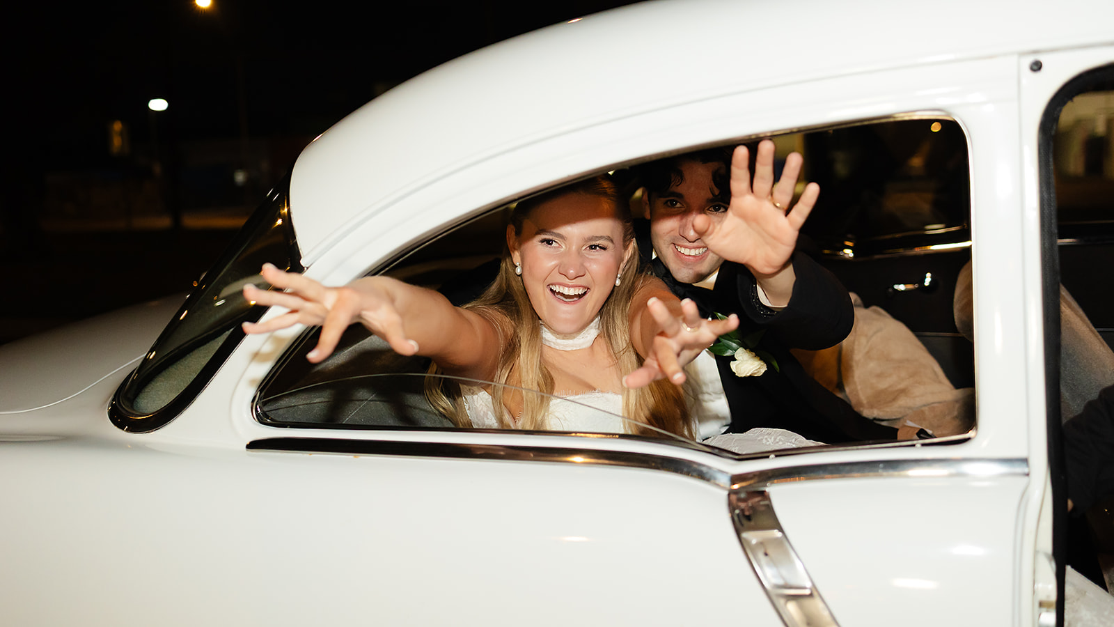 Couple leaving reception in classic getaway car at night in Phoenix
