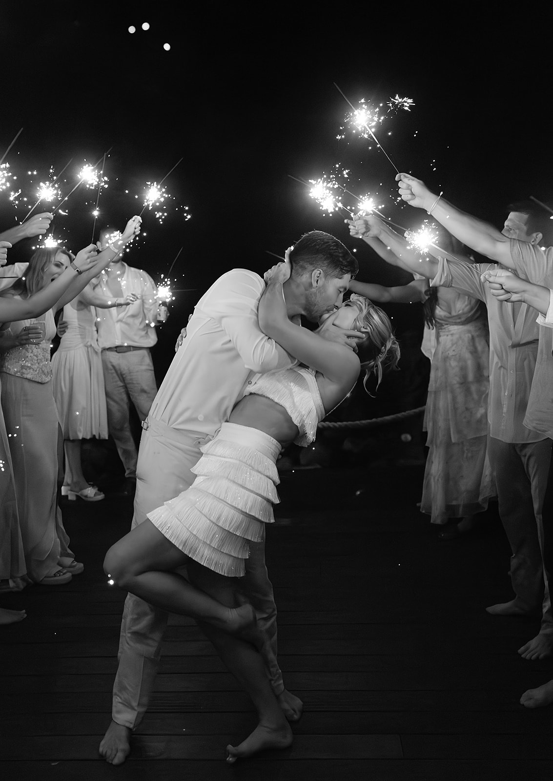 Newlyweds surrounded by guests holding sparklers at coastal villa