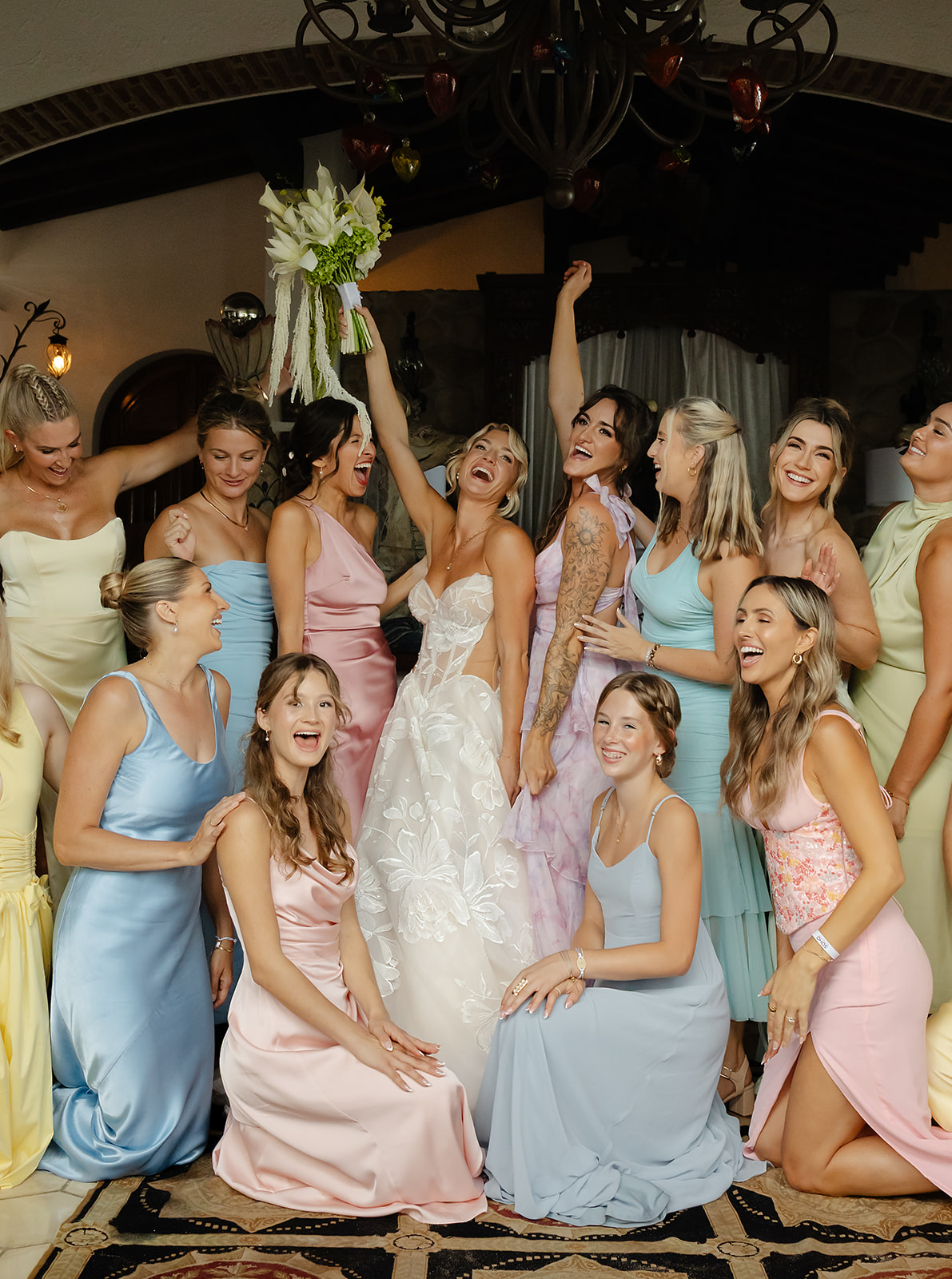 Bride getting ready with friends wearing colorful dresses in villa suite