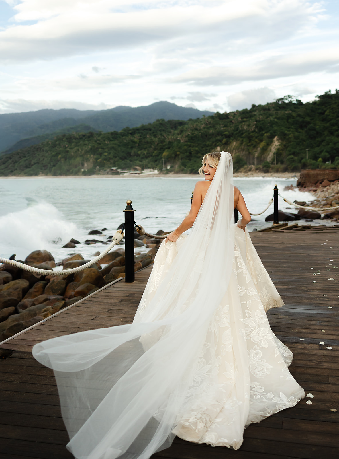 Waves crashing along rocks behind bride running and holding her dress during portraits at private villa wedding