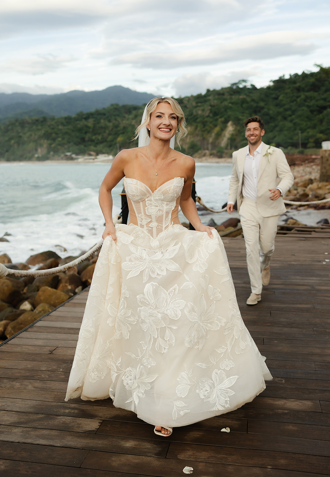 Bride holding dress while running on private villa deck overlooking the ocean in Mexico