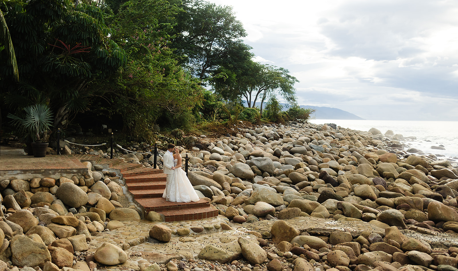 Bride and groom portrait at golden hour along rocky shoreline in Mexico